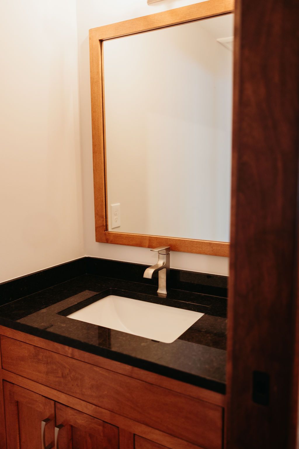 Bathroom vanity with dark countertop, white sink, wood cabinet and frame mirror.