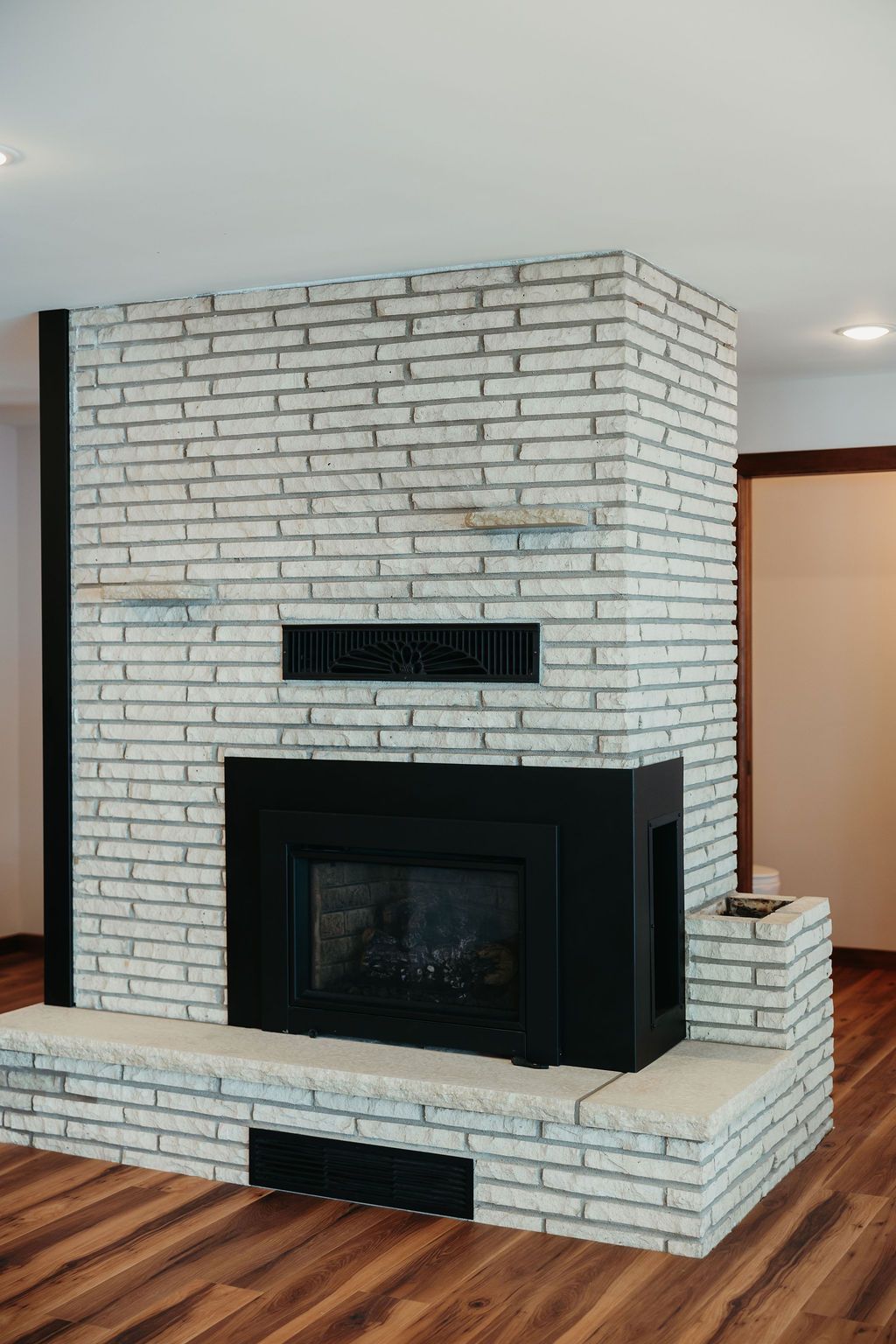 White brick fireplace with black insert, wooden floor, and a metal beam.