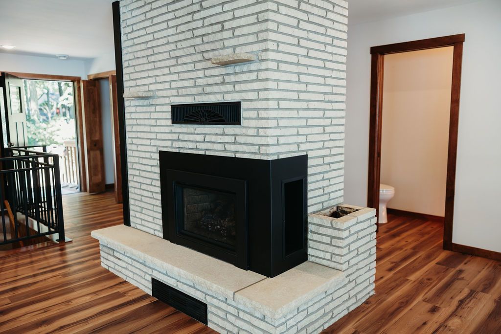 Brick fireplace in a home interior with hardwood floors. A doorway and stairway are visible.