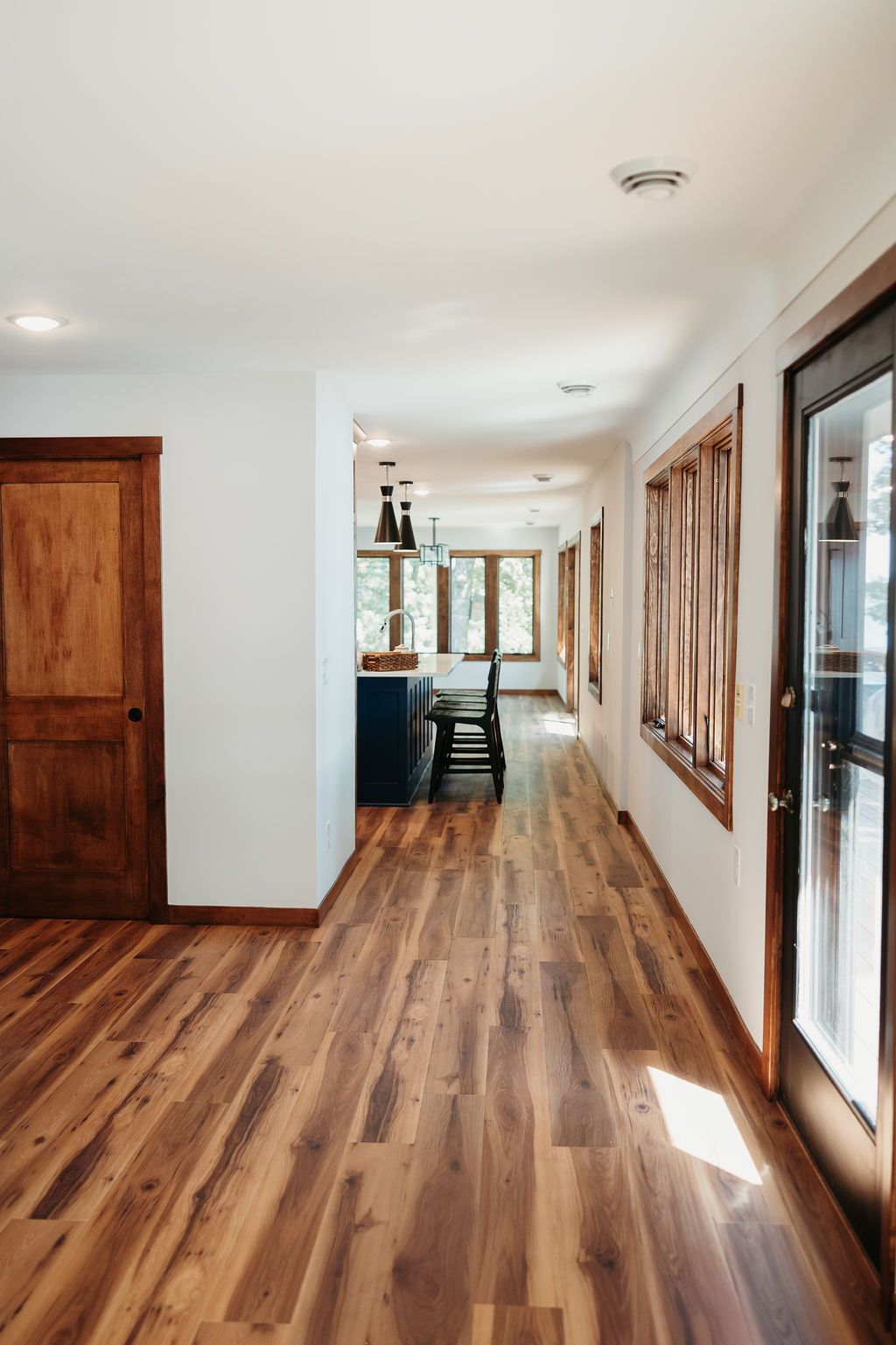 Long hallway with wooden floors, white walls, and wooden-framed doors and windows.