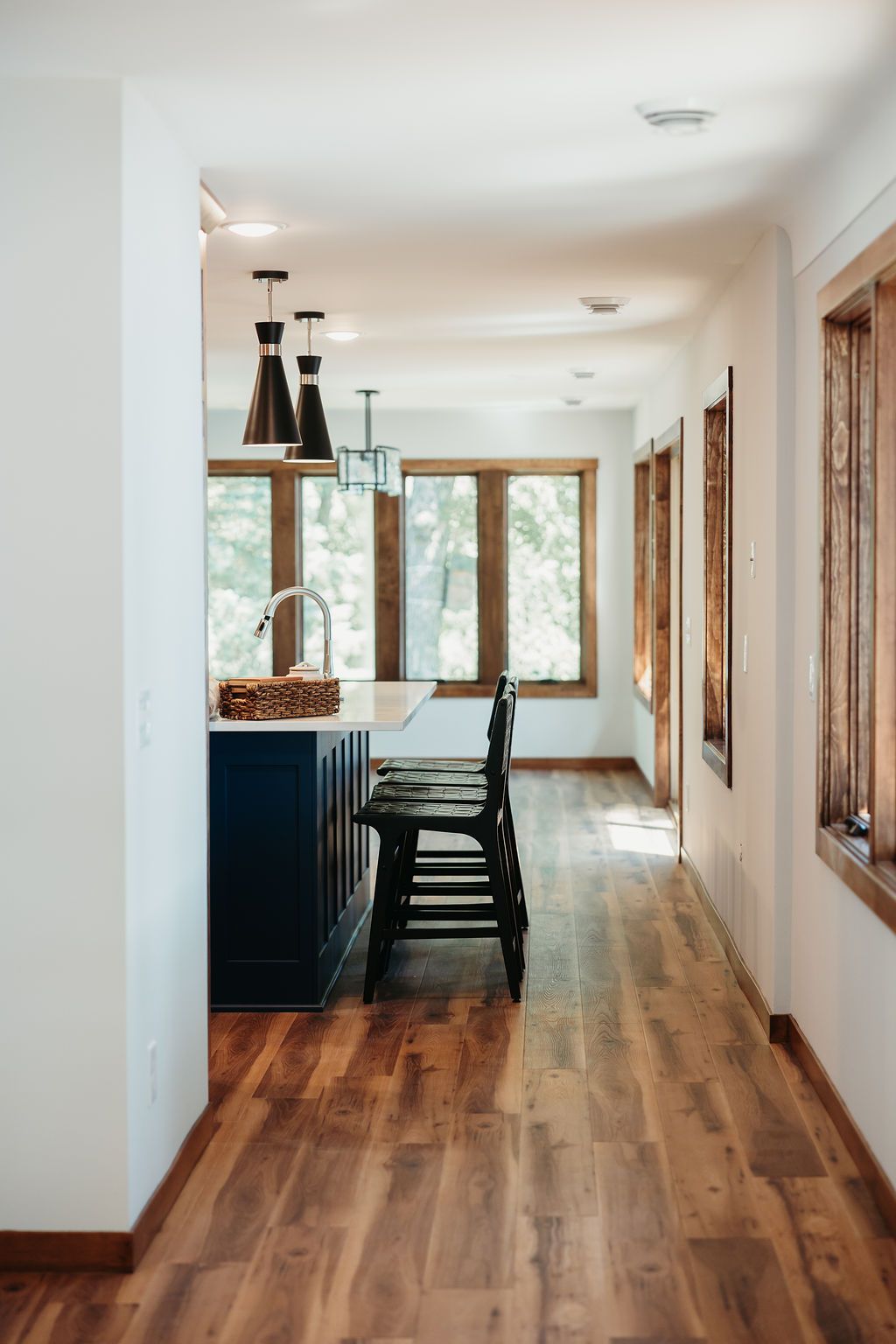 Hallway with wood floors leads to a kitchen with a blue island and wooden bar stools.