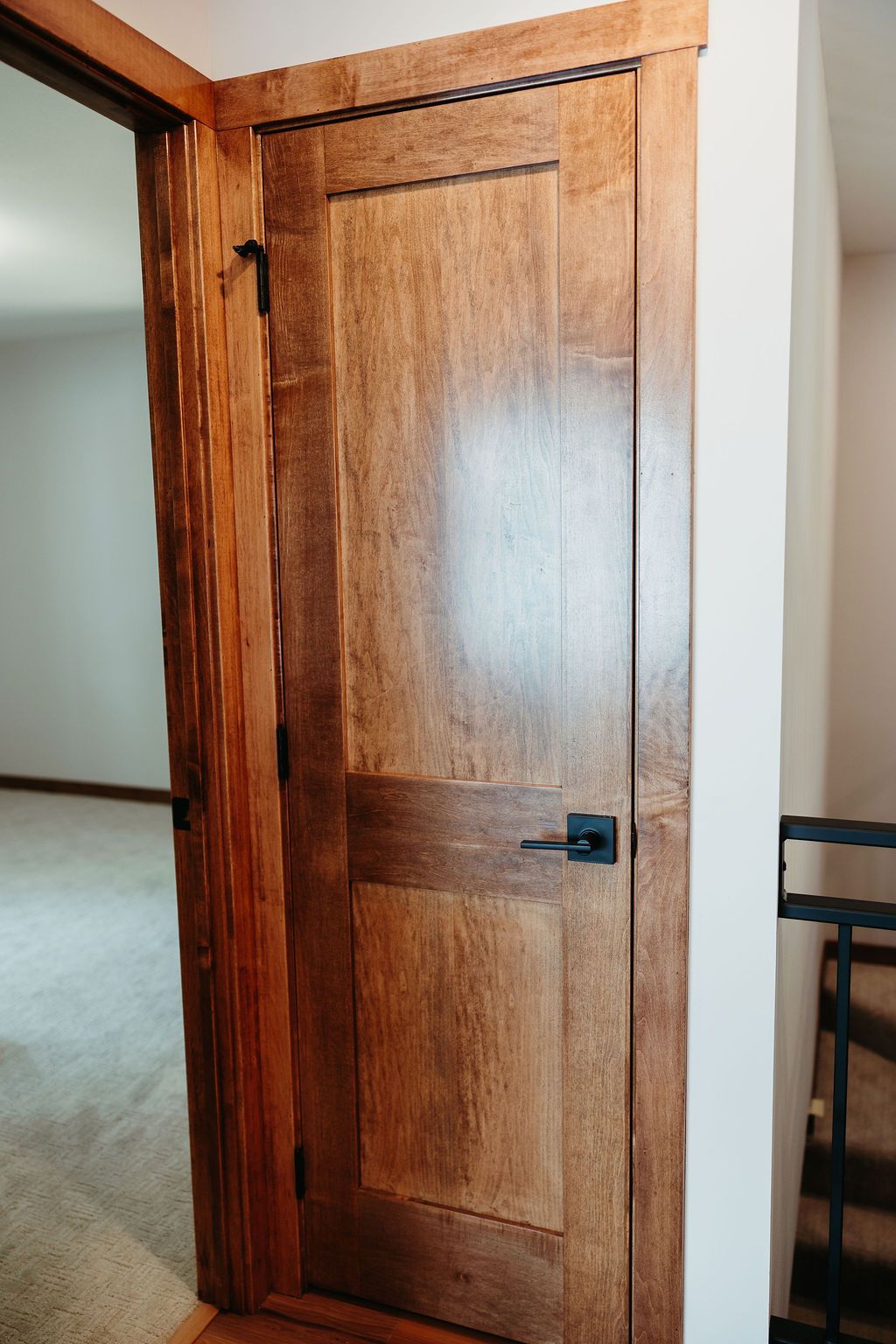 Wooden door with dark hardware, set in a light-colored frame. Opens into a room with carpet.
