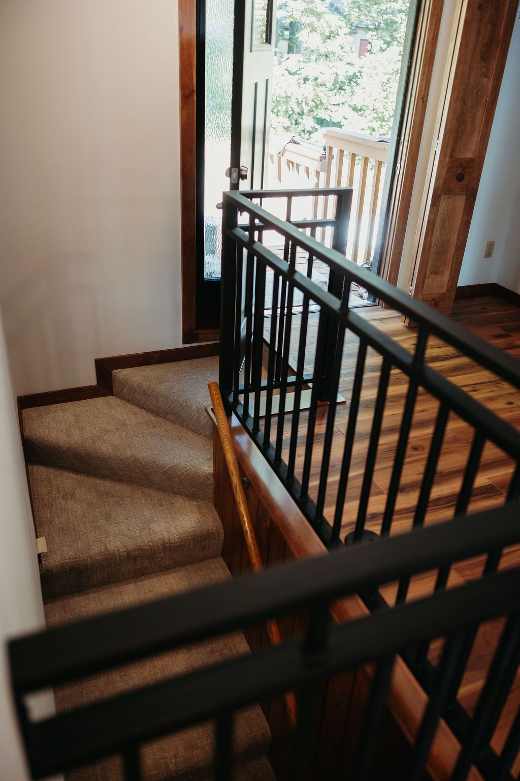Staircase with carpeted steps and black metal railings leading to a doorway. Sunlight streams in.