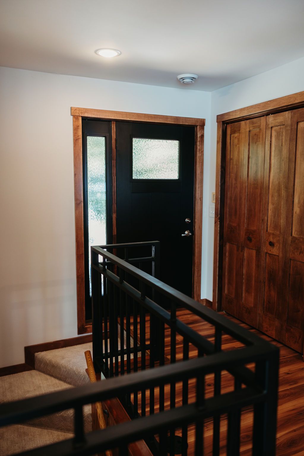Interior doorway and closet with wood trim, black door, and staircase with black railing.