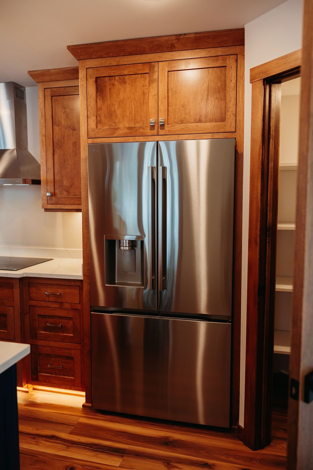 Stainless steel refrigerator with built-in wooden cabinets. Kitchen with wooden floors and a pantry door.