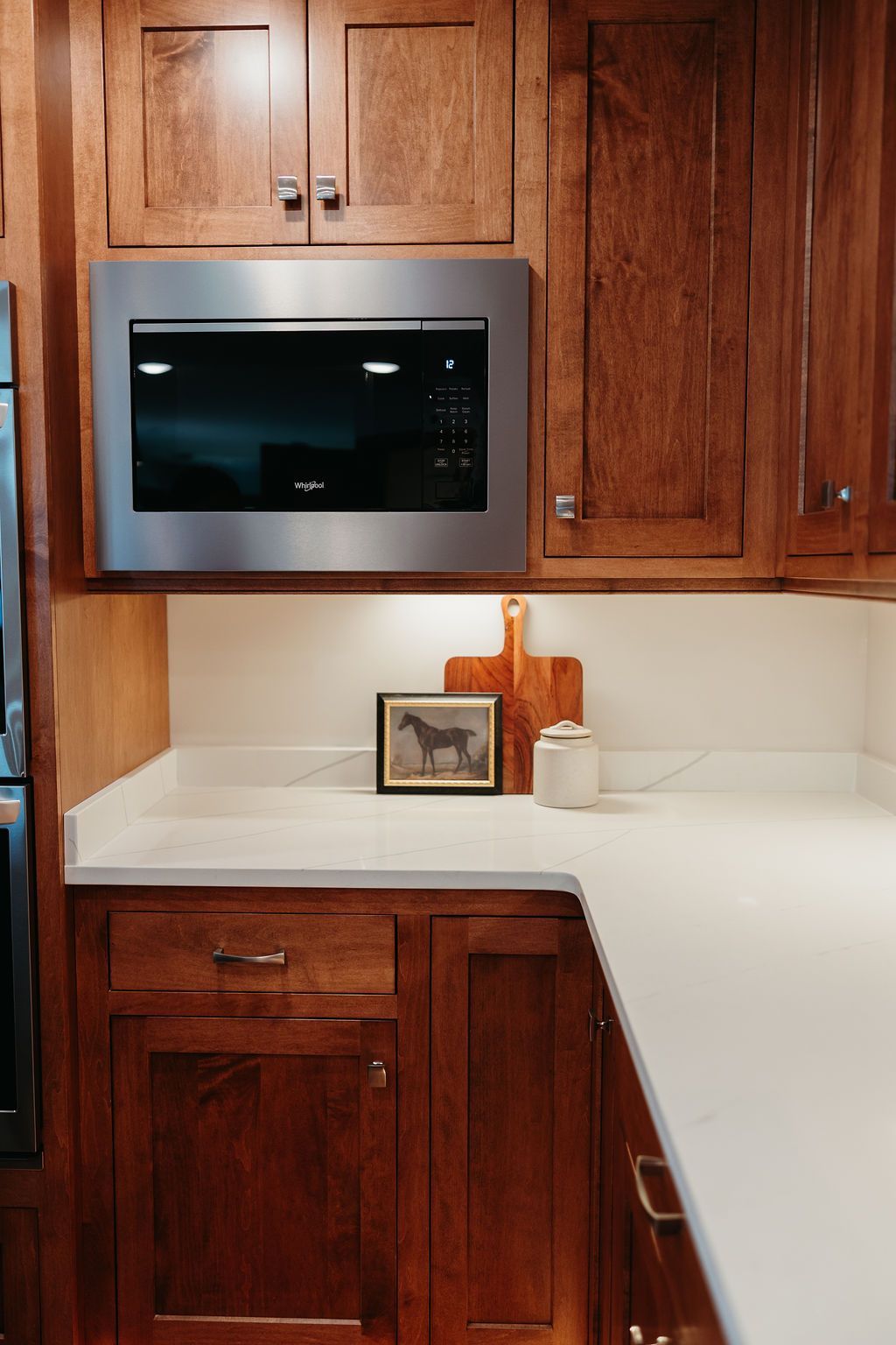 Kitchen corner with dark wood cabinets, a stainless steel microwave, and white countertops.