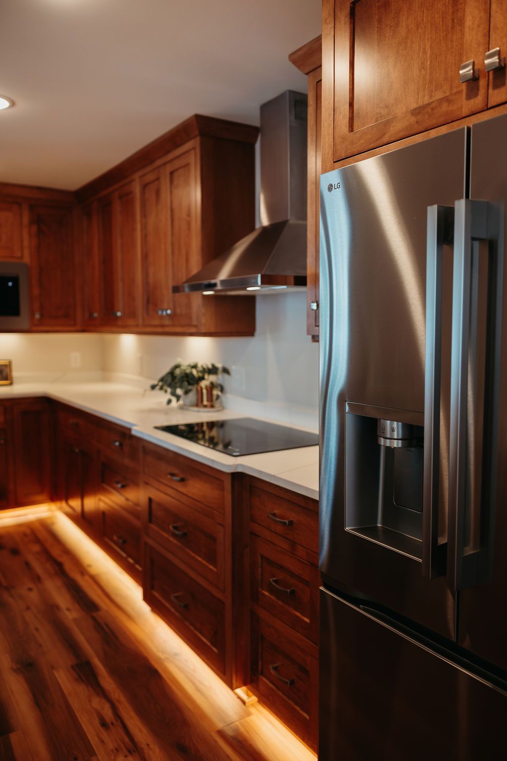 Wooden kitchen with stainless steel appliances, white countertops, and under-cabinet lighting.