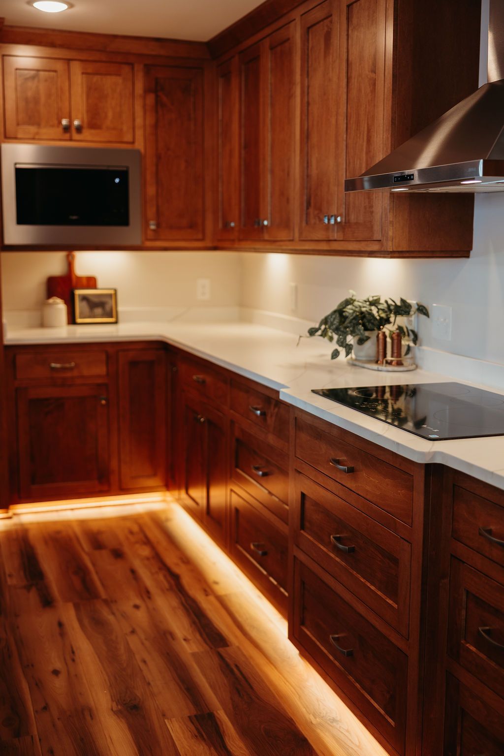 Warm-toned kitchen with wooden cabinets, white countertops, and under-cabinet lighting.