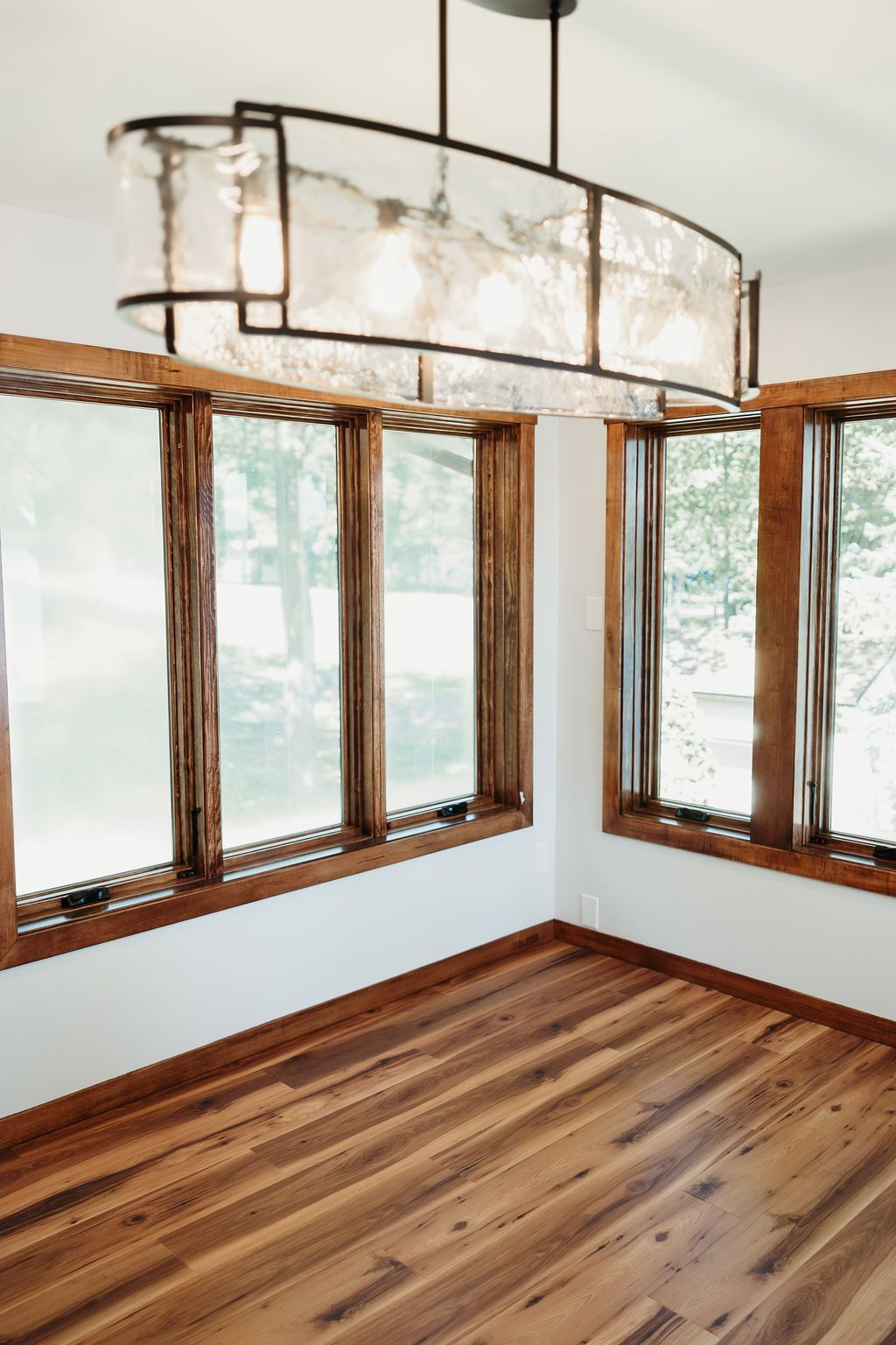 Empty room with hardwood floors, dark wood window frames, and a textured, rectangular light fixture.