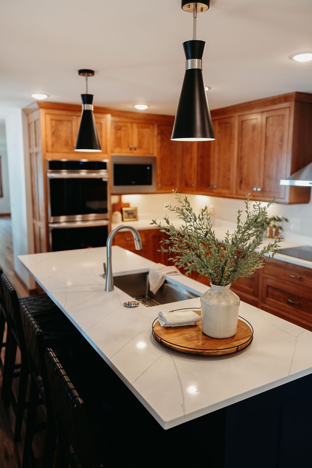 Kitchen with white countertop island, black pendant lights, and wooden cabinets.