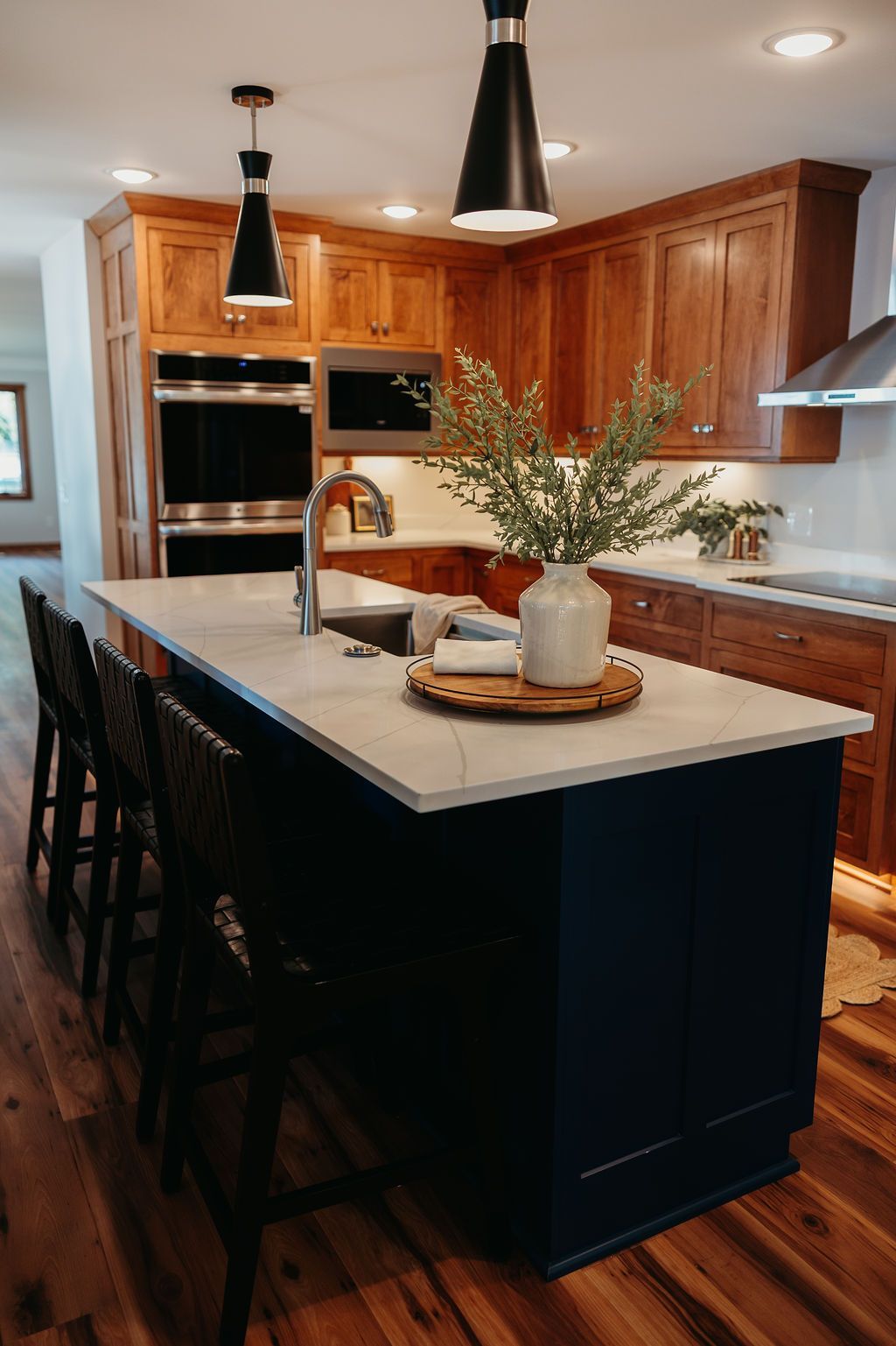 Kitchen with a navy island, wood cabinets, and marble countertop. Black pendant lights hang above.