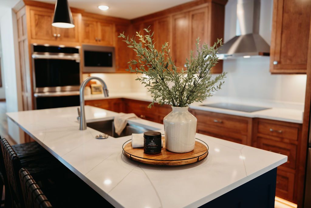 Kitchen island with a wooden tray, flowers, and a sink; surrounding cabinets are wood.
