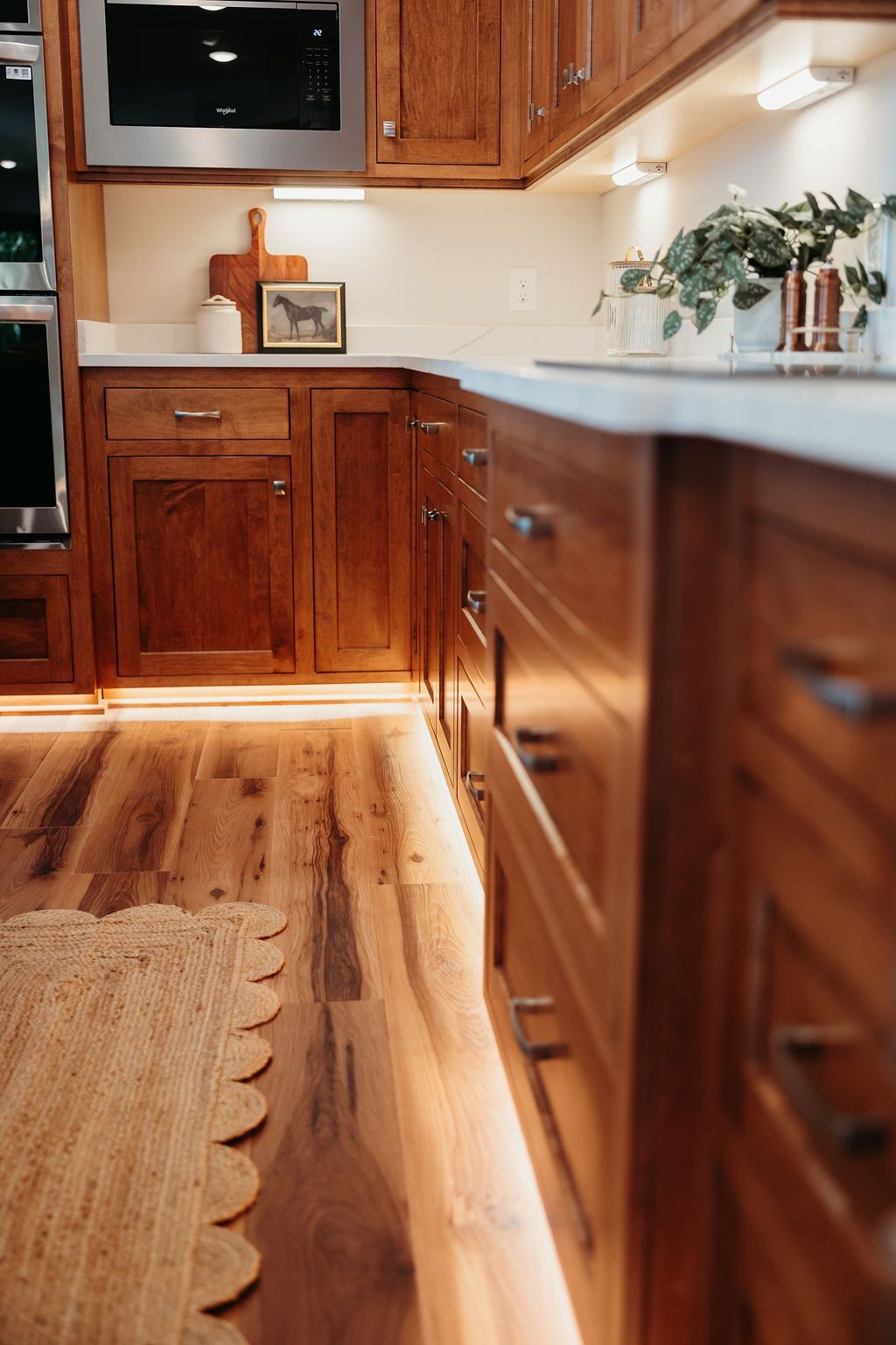Wooden kitchen cabinets with under-cabinet lighting. Light wood flooring and white countertops.