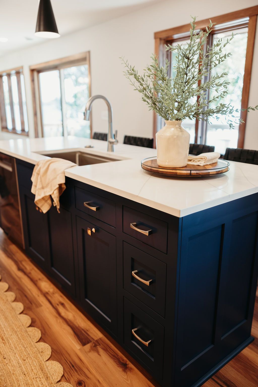 Navy blue kitchen island with white countertop, sink, and gold hardware. Vase of greenery on top.