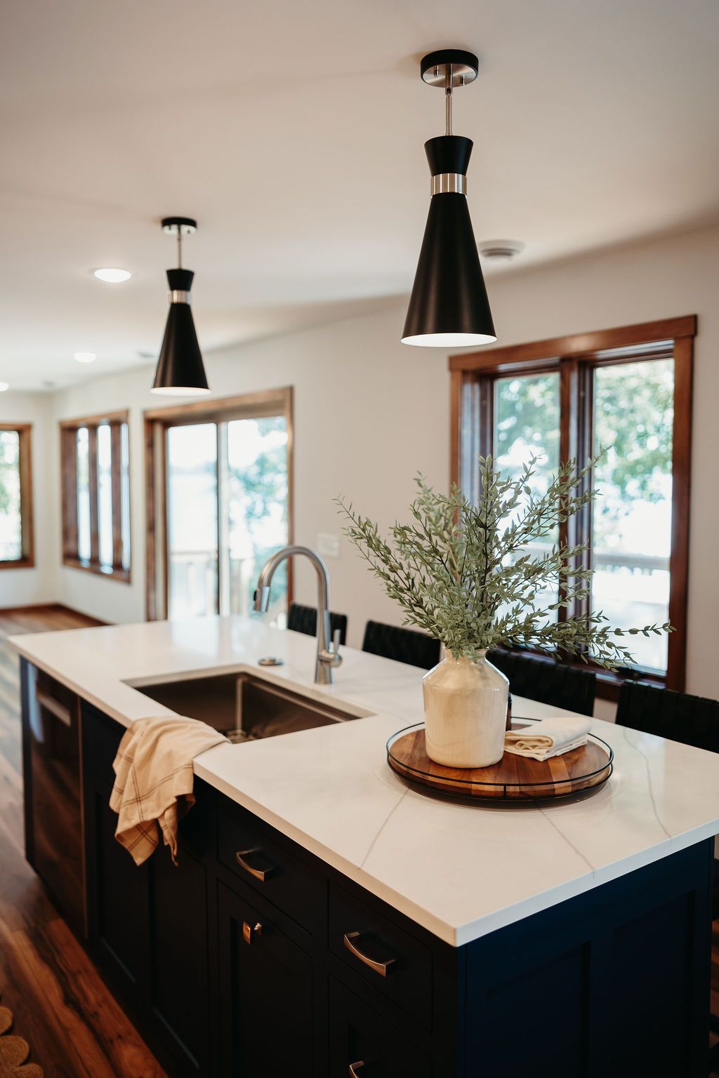 Kitchen island with black cabinets, white countertop, sink, and pendant lights. Vase with greenery.