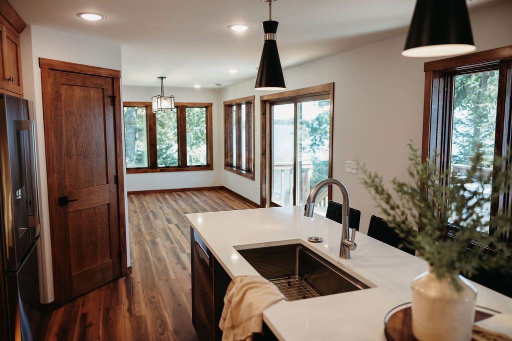 Kitchen with island, sink, dark cabinets, and hardwood floors; living area with windows and view.