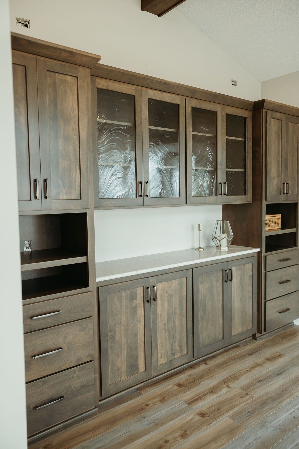 Built-in dark wood cabinetry with glass-fronted upper cabinets, white countertop, and light wood flooring.