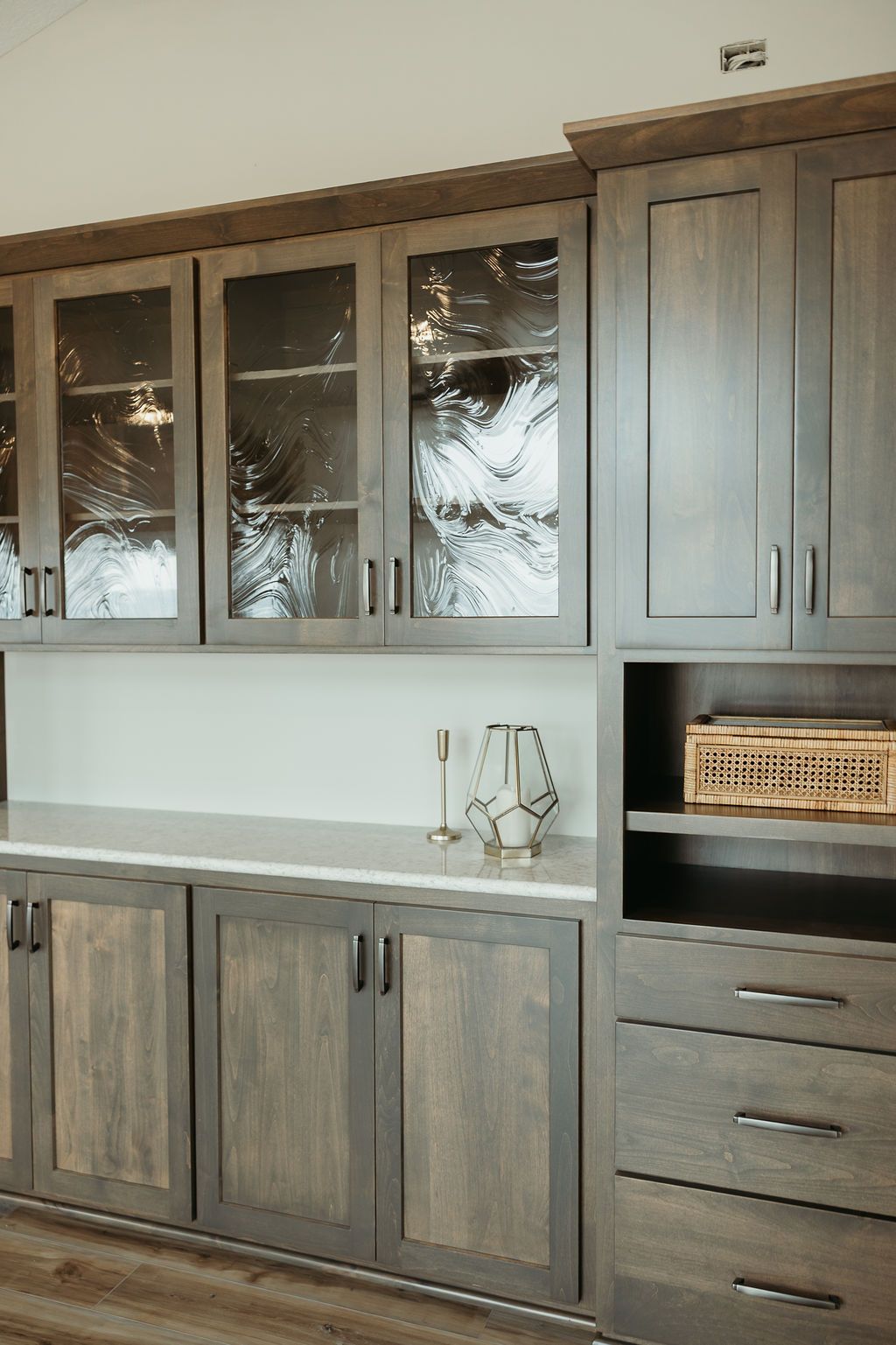 Gray and brown cabinets with glass-paneled upper doors. Neutral countertops and decorative objects.