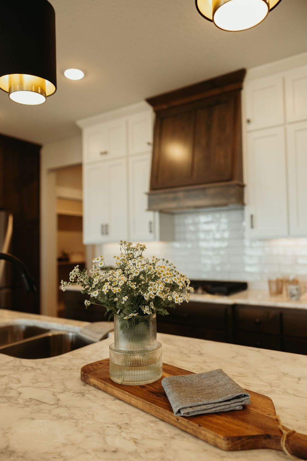 Kitchen counter with vase of flowers, cutting board, and a gray cloth. 