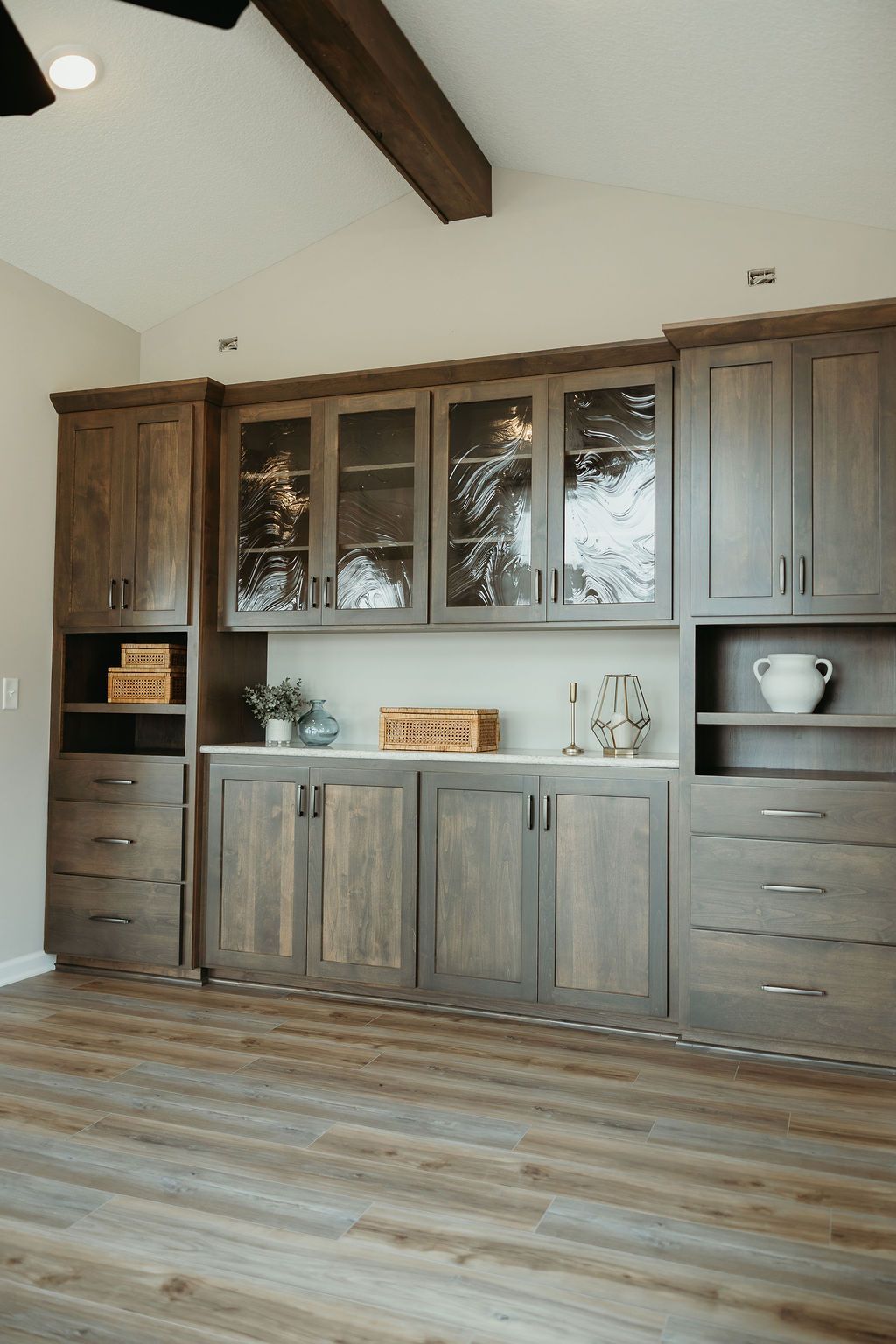 Wooden cabinetry with glass-front uppers and white countertop in a room with wood-look flooring.