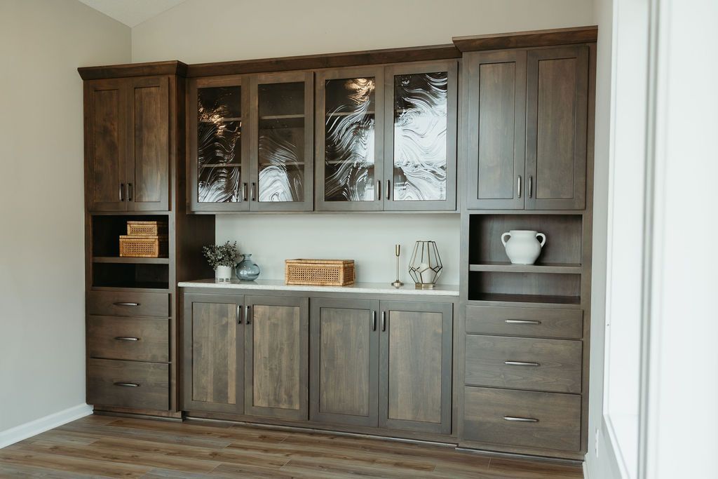 Built-in wood cabinetry with glass-front display cabinets, open shelves, and drawers, against a neutral wall.