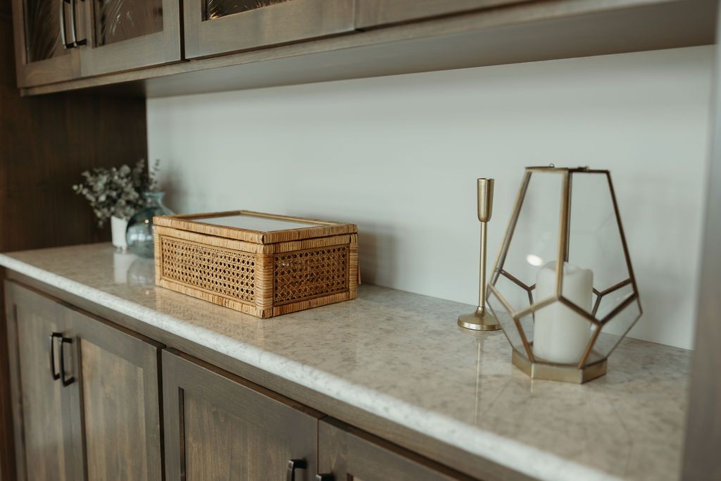 Countertop with decorative items: woven box, candleholder, geometric lantern, and cabinets.