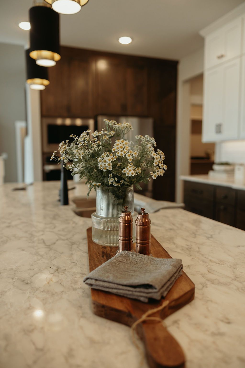 Kitchen island with flowers, cutting board, salt/pepper shakers, and folded cloth on a marble countertop.
