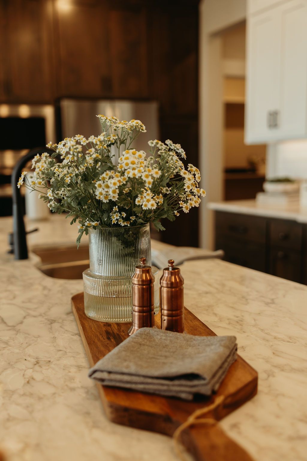 Kitchen island with flowers, copper spice jars, and a folded cloth on a wooden board.