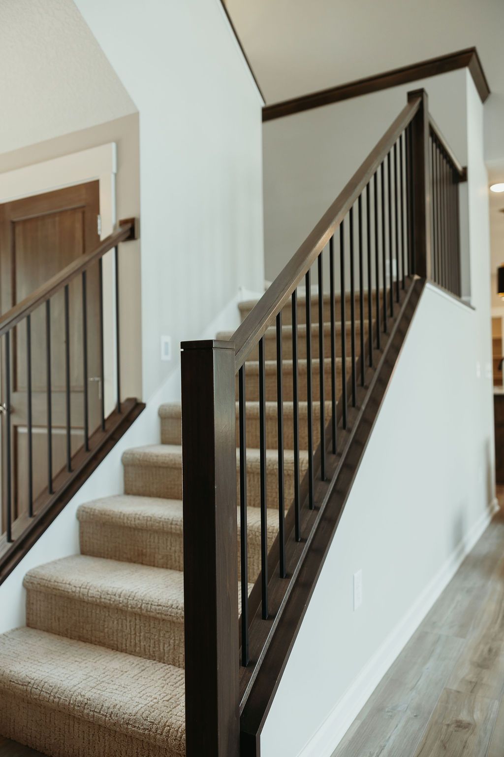 Staircase with brown banisters and carpeted steps against a white wall.