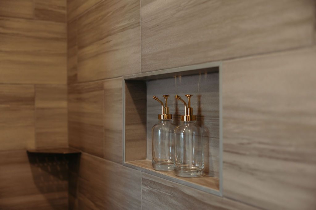 Shower niche with three clear bottles, gold dispensers, and beige tile.