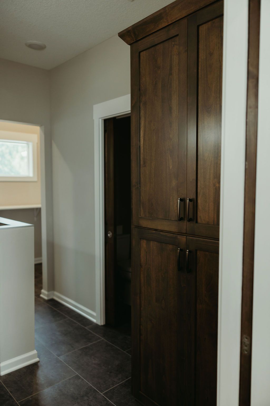 Tall, dark wooden pantry cabinet with two doors, on a dark tiled floor, next to a doorway.
