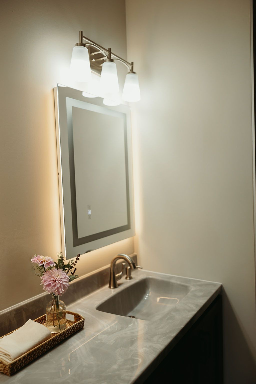 Bathroom vanity with lighted mirror, sink, and decorative flowers.