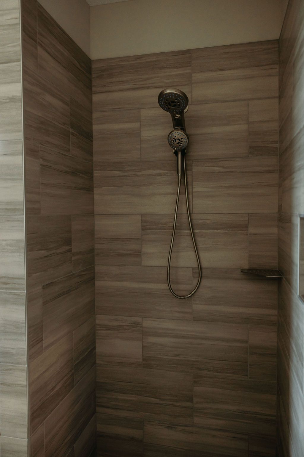Shower with brown wood-look tiles. A decorative showerhead with a handheld option hangs in the center.