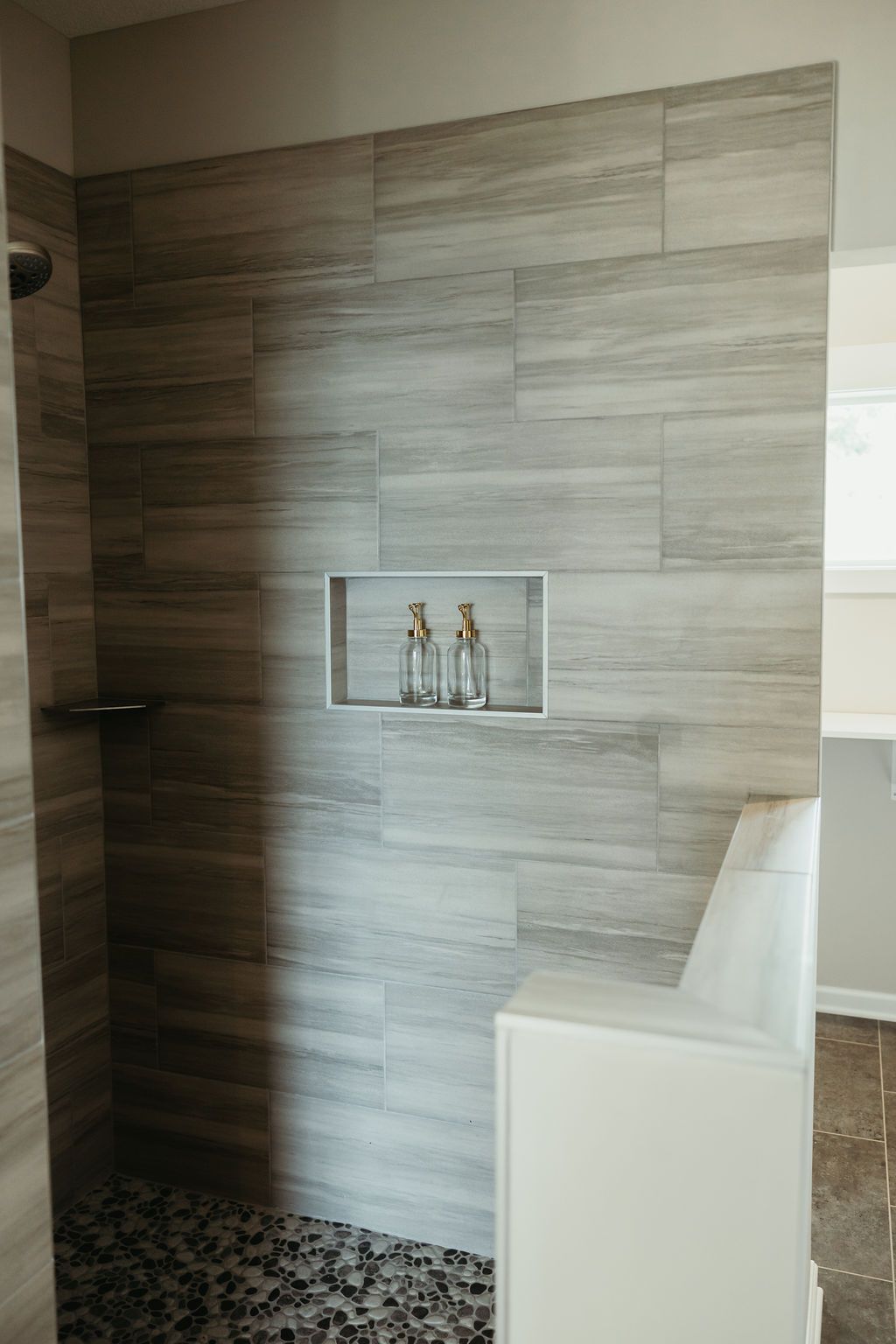 A walk-in shower with gray wood-look tiles, a built-in shelf, and a bench.