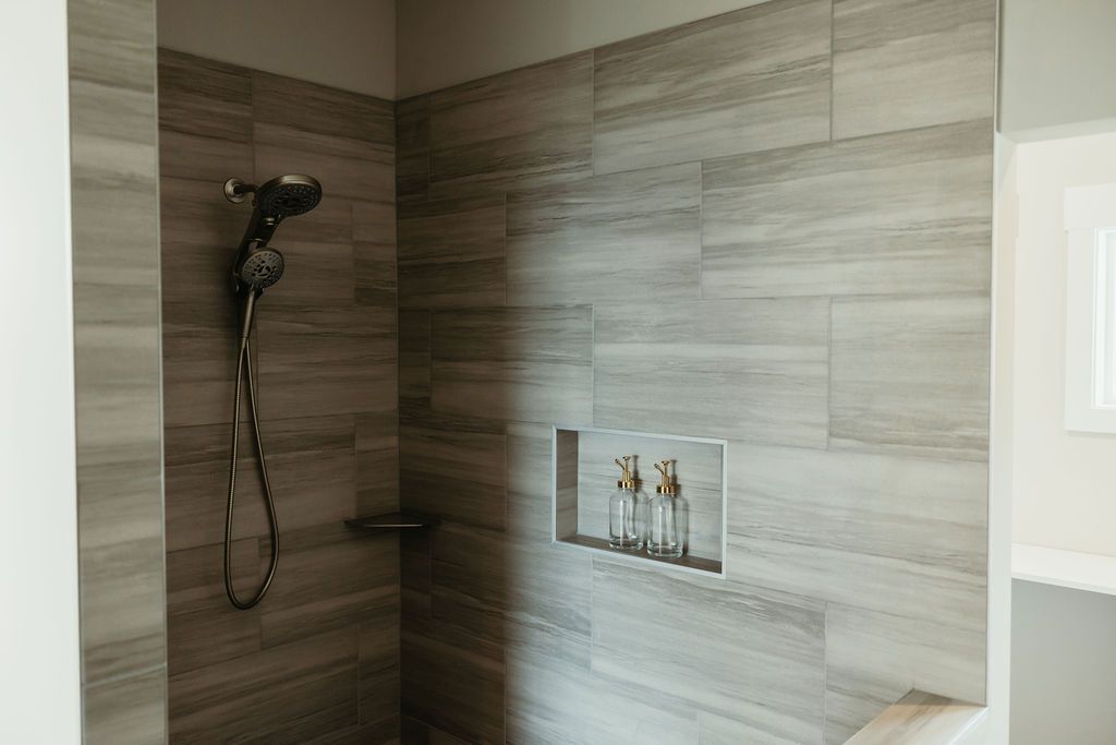 Shower with gray wood-look tile, dark shower head, built-in shelf and niche for toiletries.