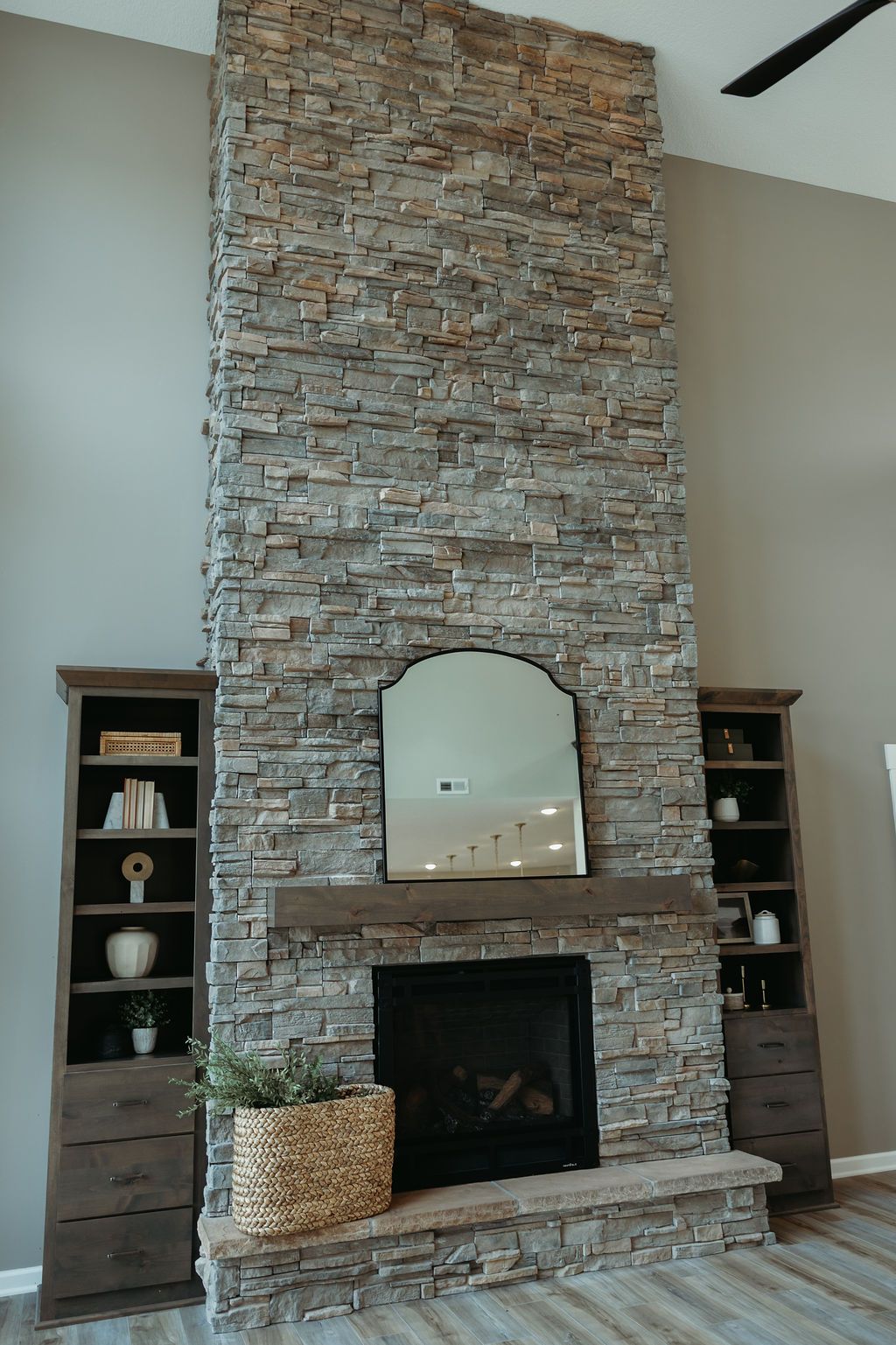Stone fireplace with mirror and wooden mantel, flanked by bookshelves in a modern living room.