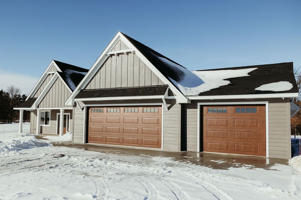 Two-car garage with brown doors and gray siding, snow on roof, winter setting.