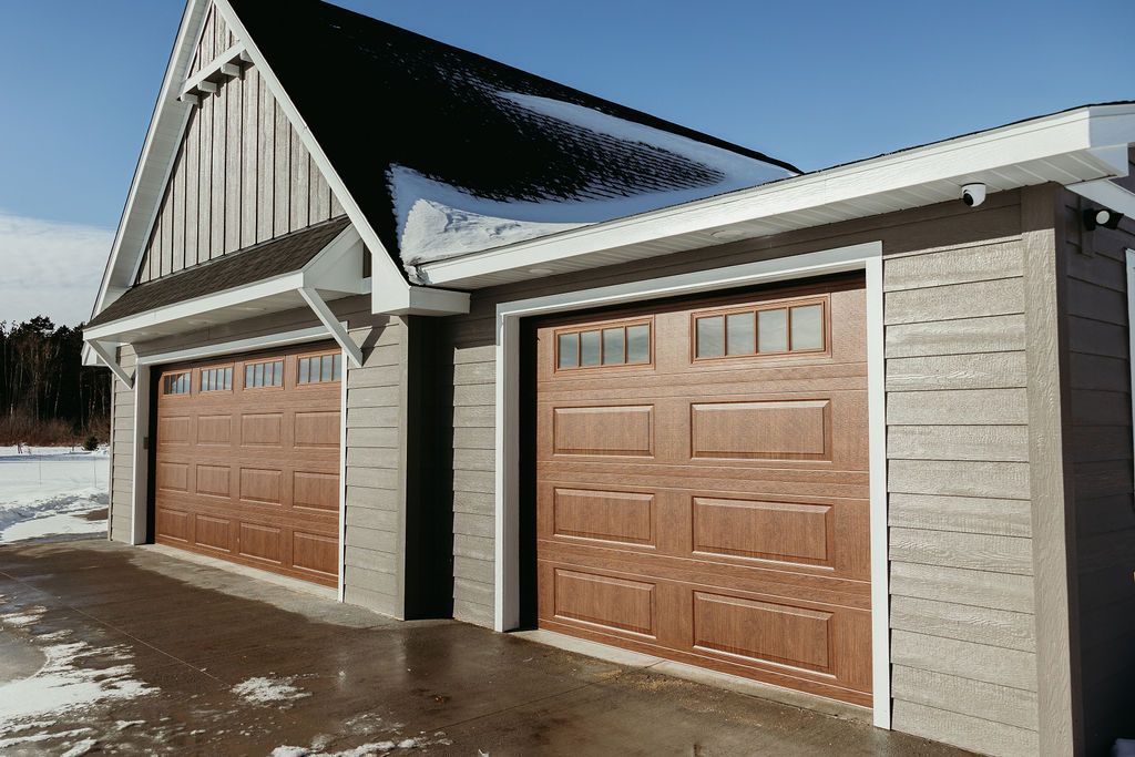Brown double garage with snow-covered roof and trim, against a blue sky.