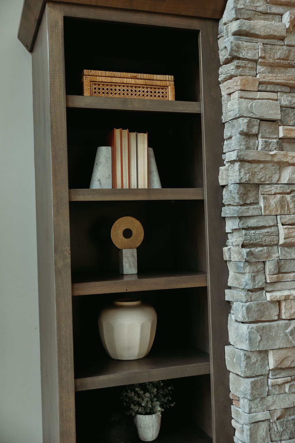 Wooden bookshelf with decorative items: books, a basket, vase, and sculpture.