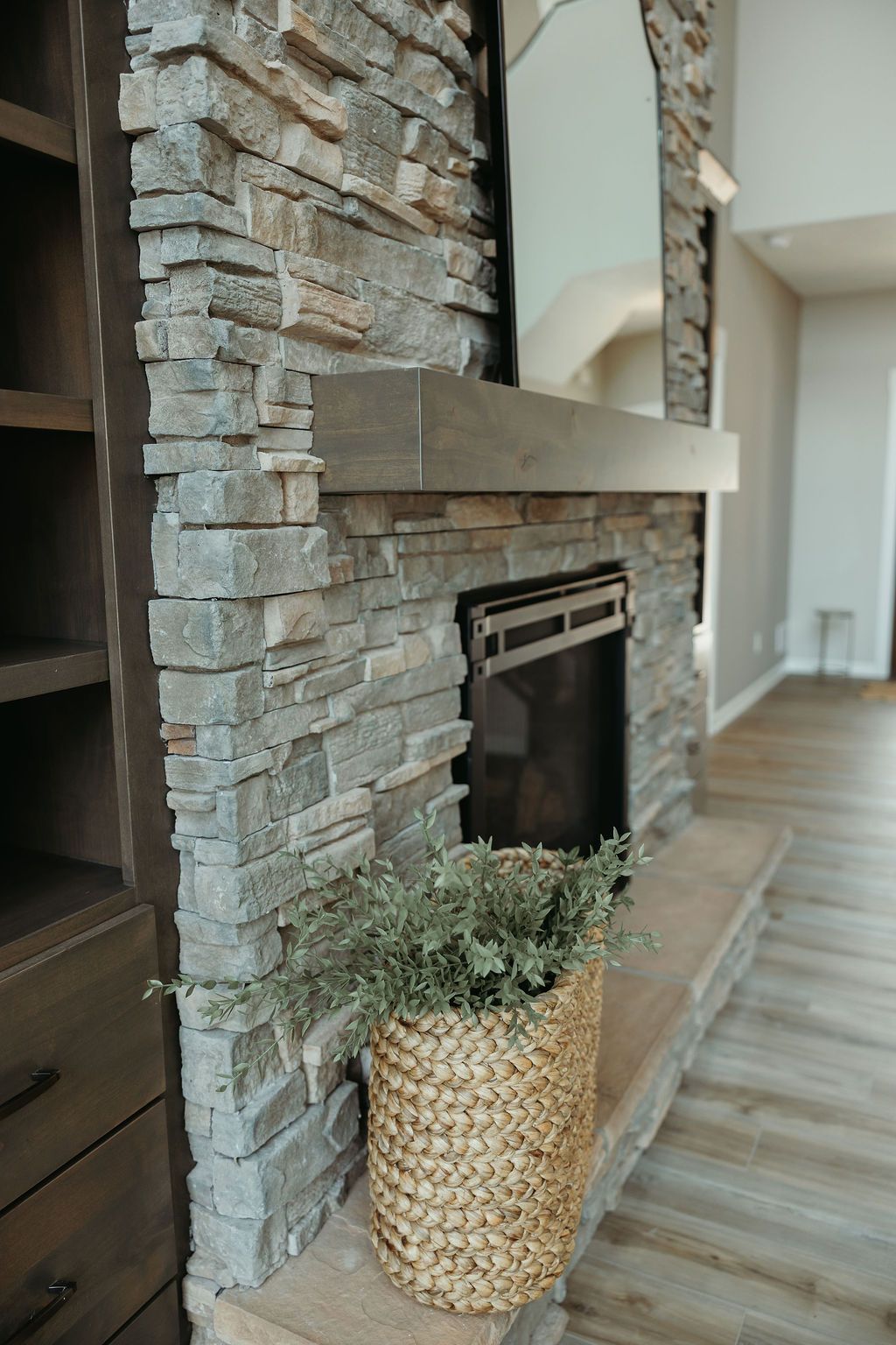 Stone fireplace with wooden mantel, built-in shelving, and a basket of greenery.