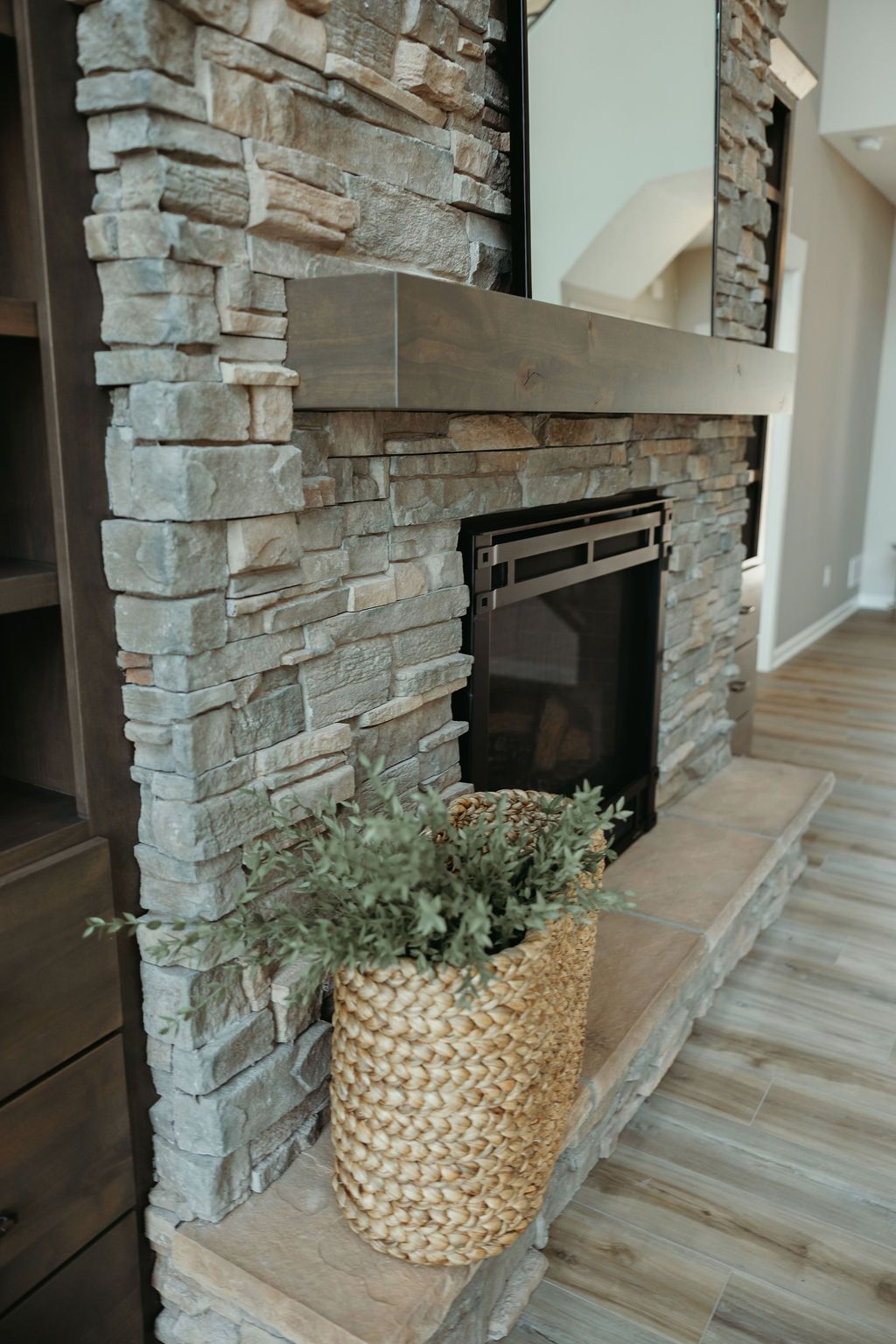 Stone fireplace with wooden mantel and woven basket of greenery.