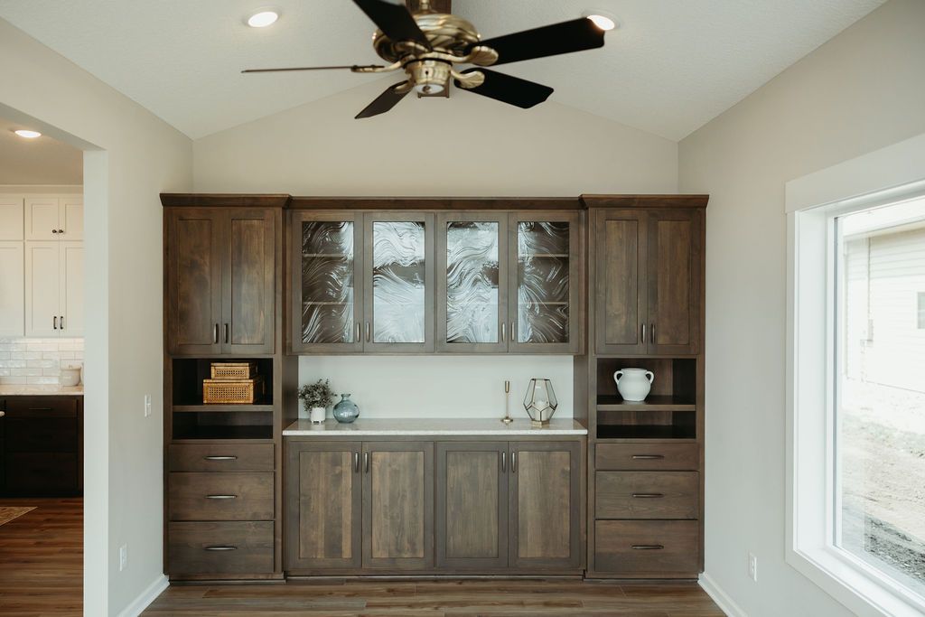 Dark wood cabinetry with glass-fronted upper cabinets and a built-in countertop in a room with a ceiling fan.