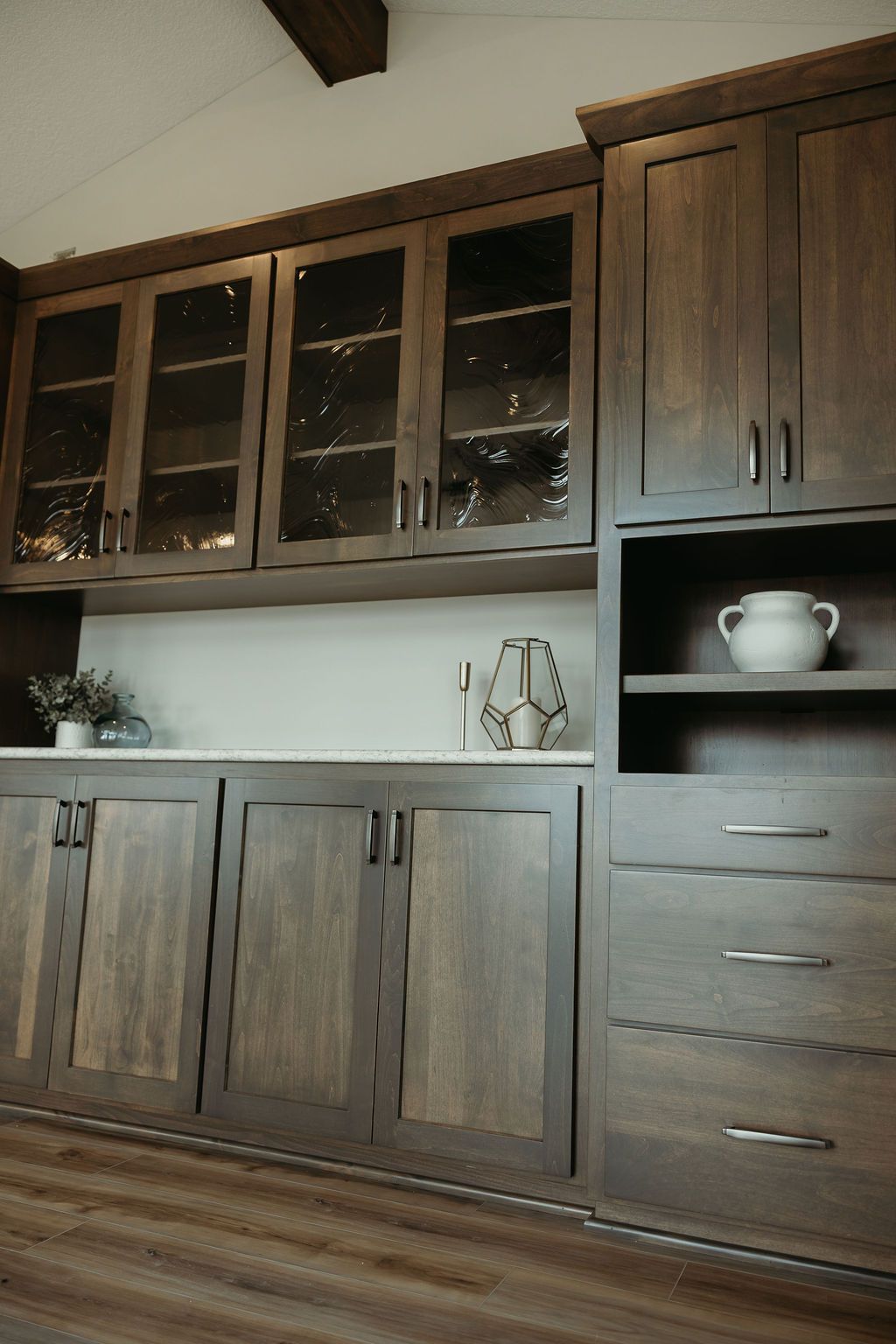 Dark wood kitchen cabinets with glass-front uppers, light countertop, and a built-in shelf.