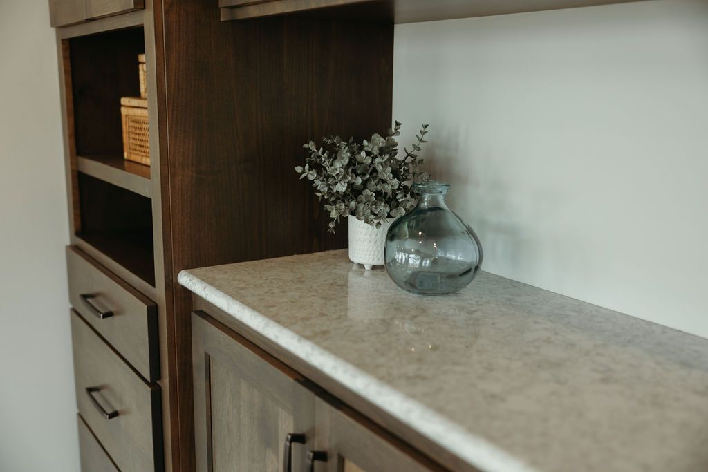 Built-in wooden cabinetry with a light countertop. A vase with greenery and a clear glass container sit on the countertop.