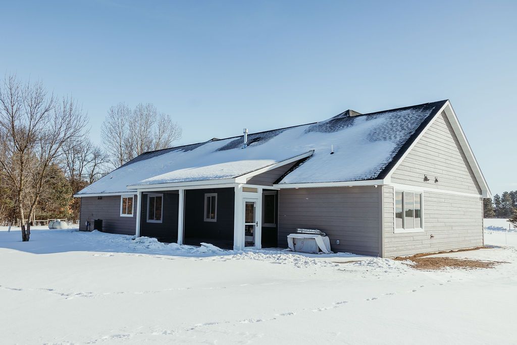 A one-story house with a snowy roof, surrounded by snow, under a clear blue sky.