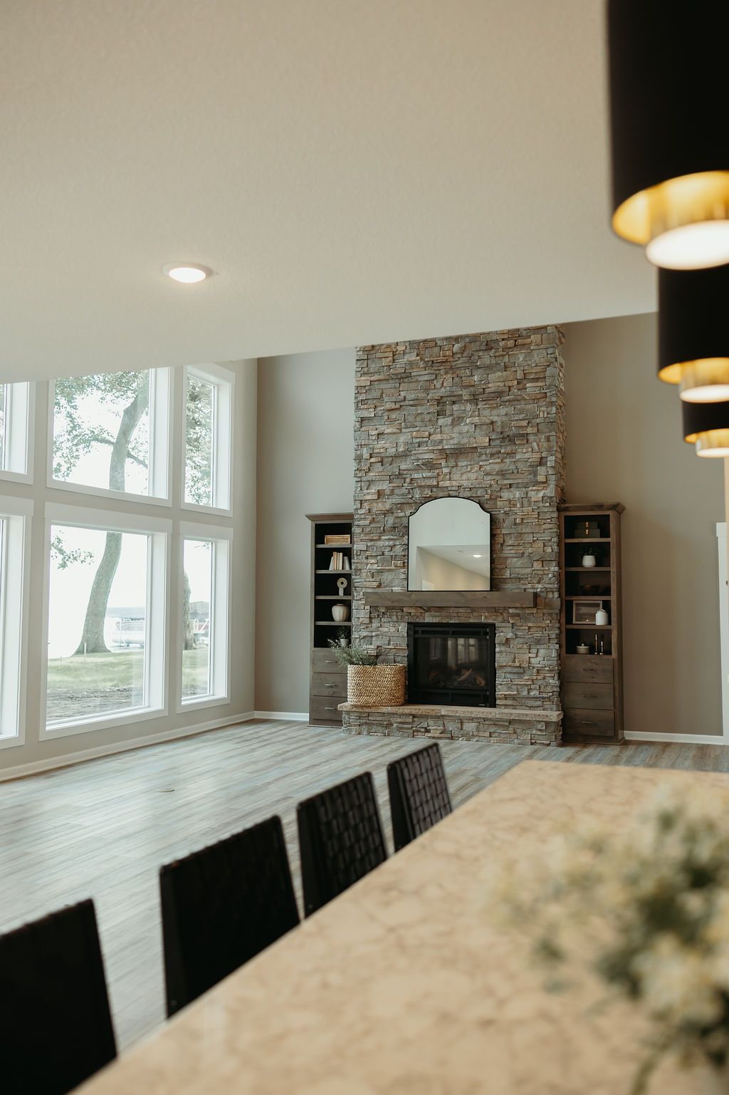 Living room with stone fireplace, large windows overlooking water, and dining area with black chairs.