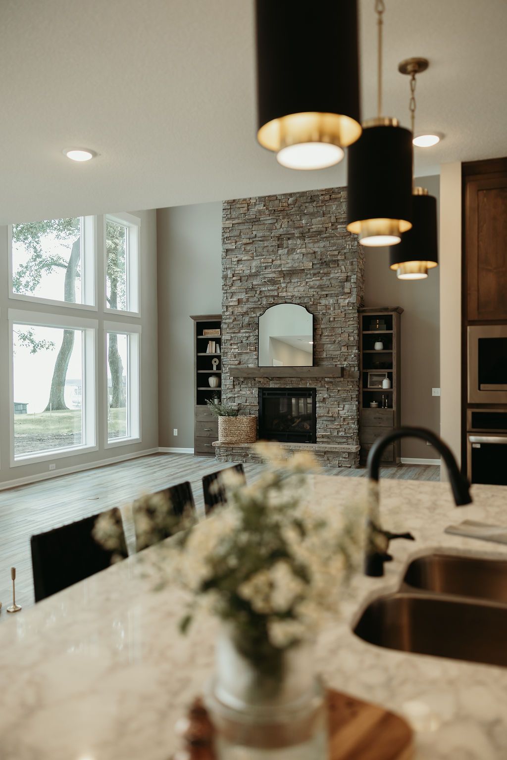 Modern kitchen with a stone fireplace, large windows overlooking a lake, and pendant lights.