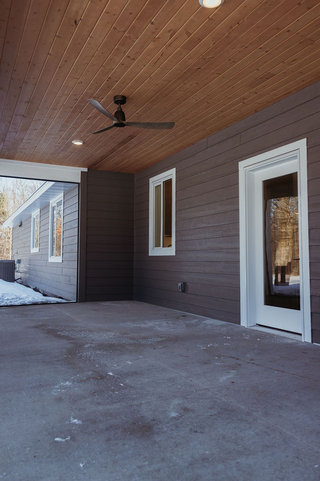 Covered patio with wood ceiling, gray walls, concrete floor, and a black ceiling fan.