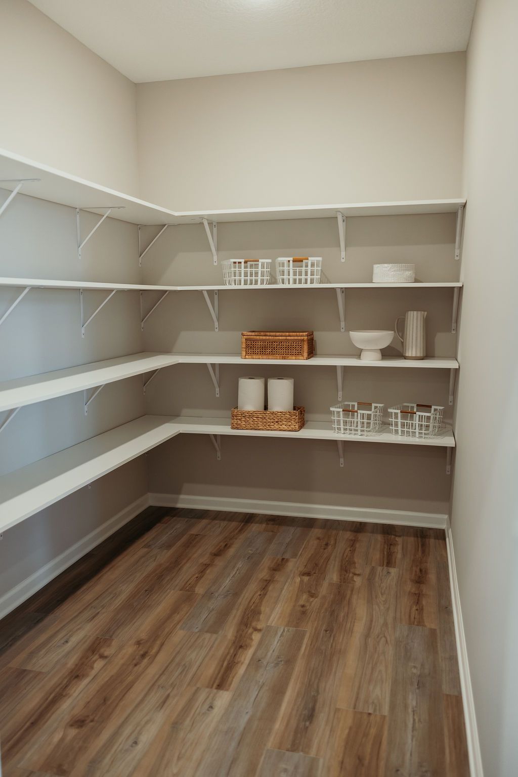 Empty pantry with wood-look flooring and white shelving on three walls, some items on shelves.
