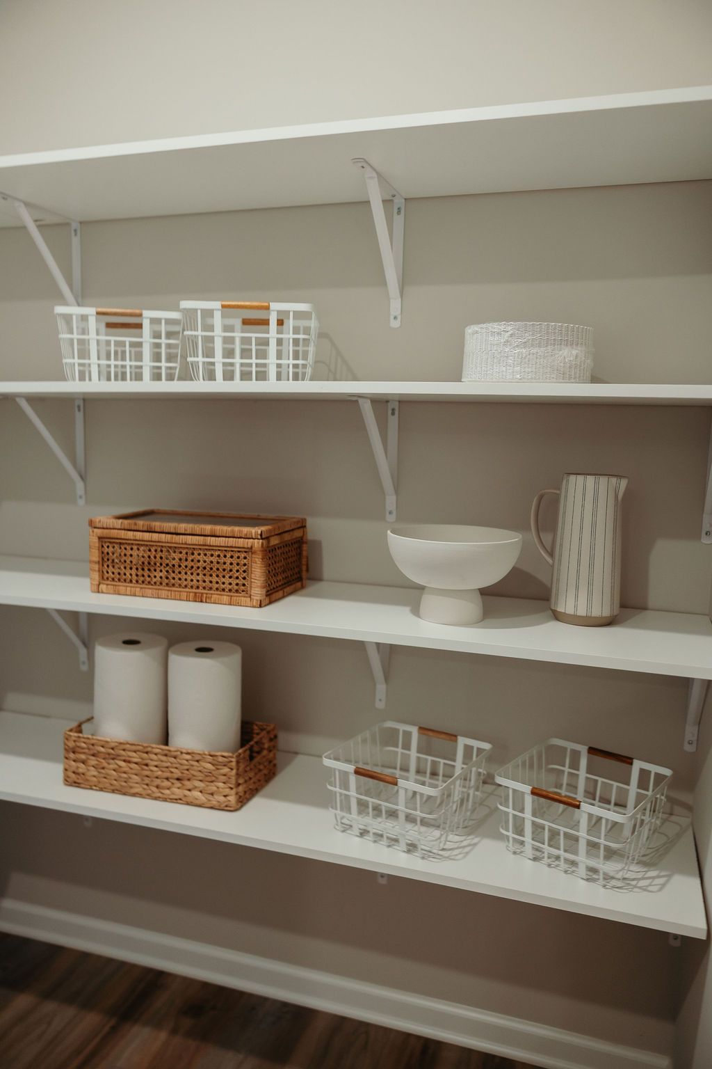 White pantry shelves with various white and wicker baskets, a pitcher, and a bowl.